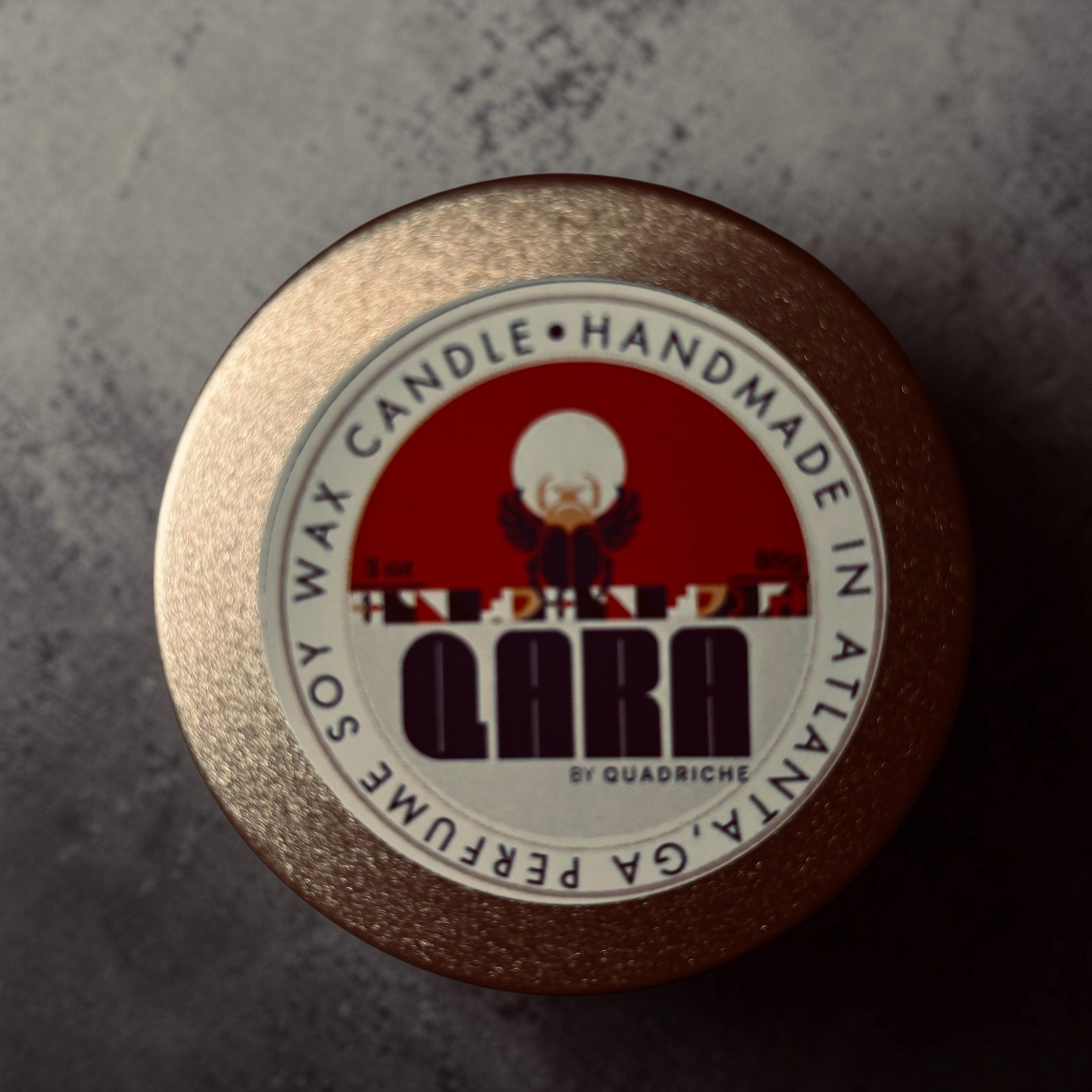 Ambrosia  QARA by Quadriche Discovery Travel 3oz Candle in a tin with a label on a concrete surface cherry blossom  fragrance scent