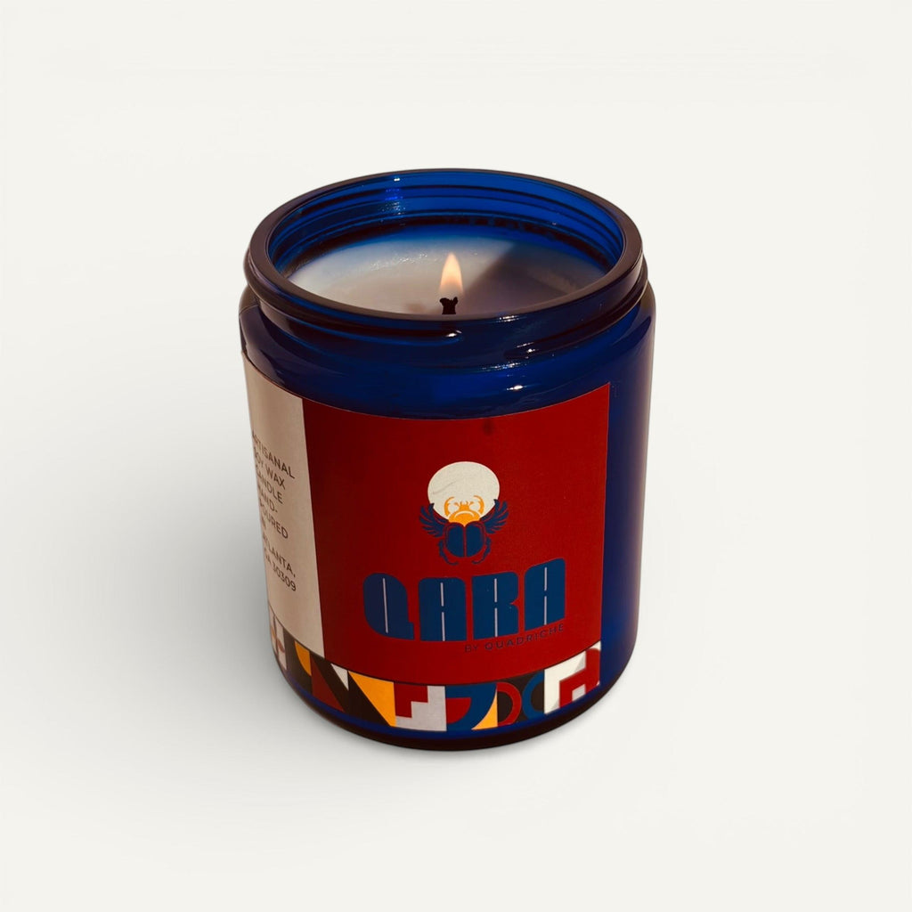 Candle in a decorative cobalt blue glass jar with a blue lid and colorful label on a white background