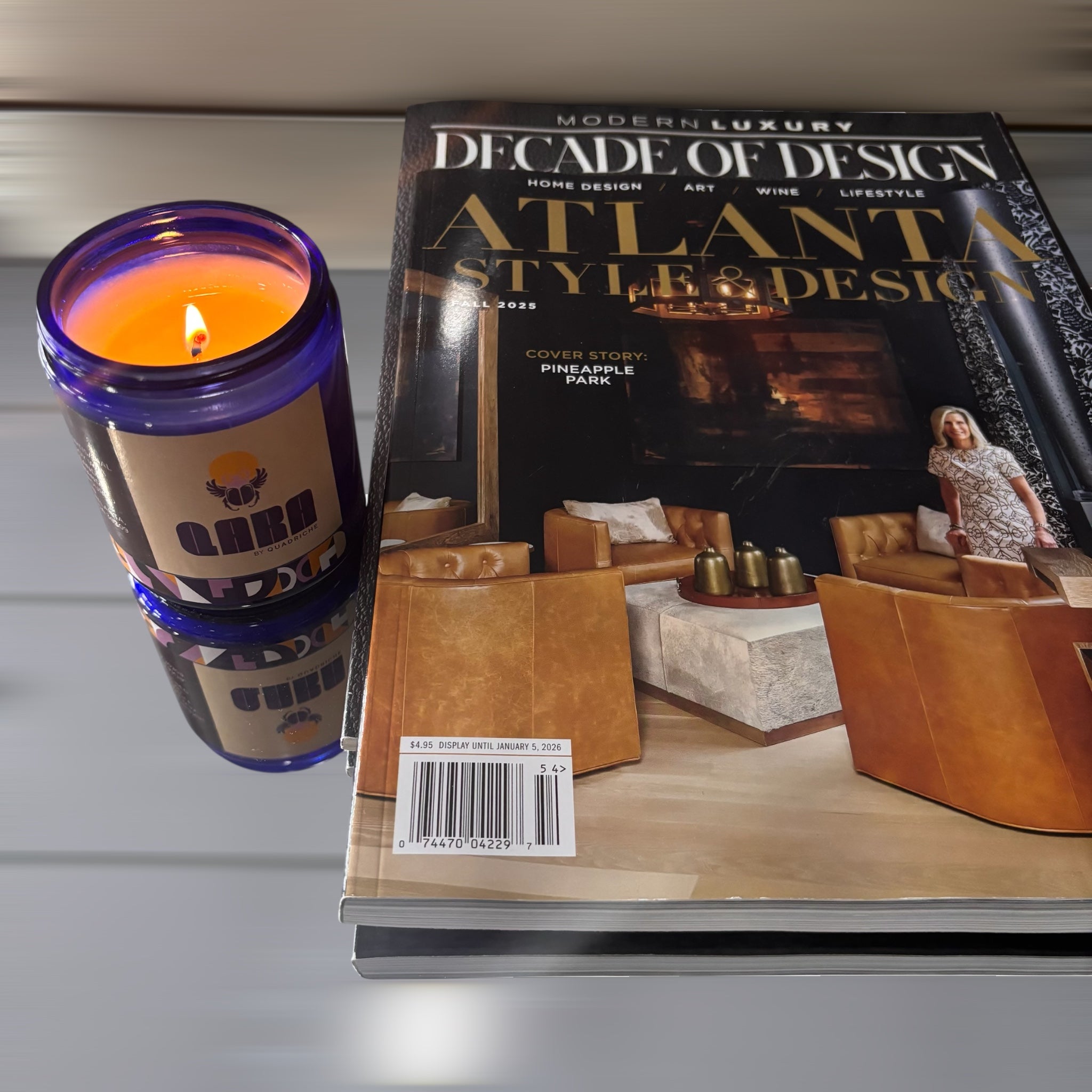 QARA Candle and magazine titled 'Modern Luxury: Decade of Design' on a reflective surface