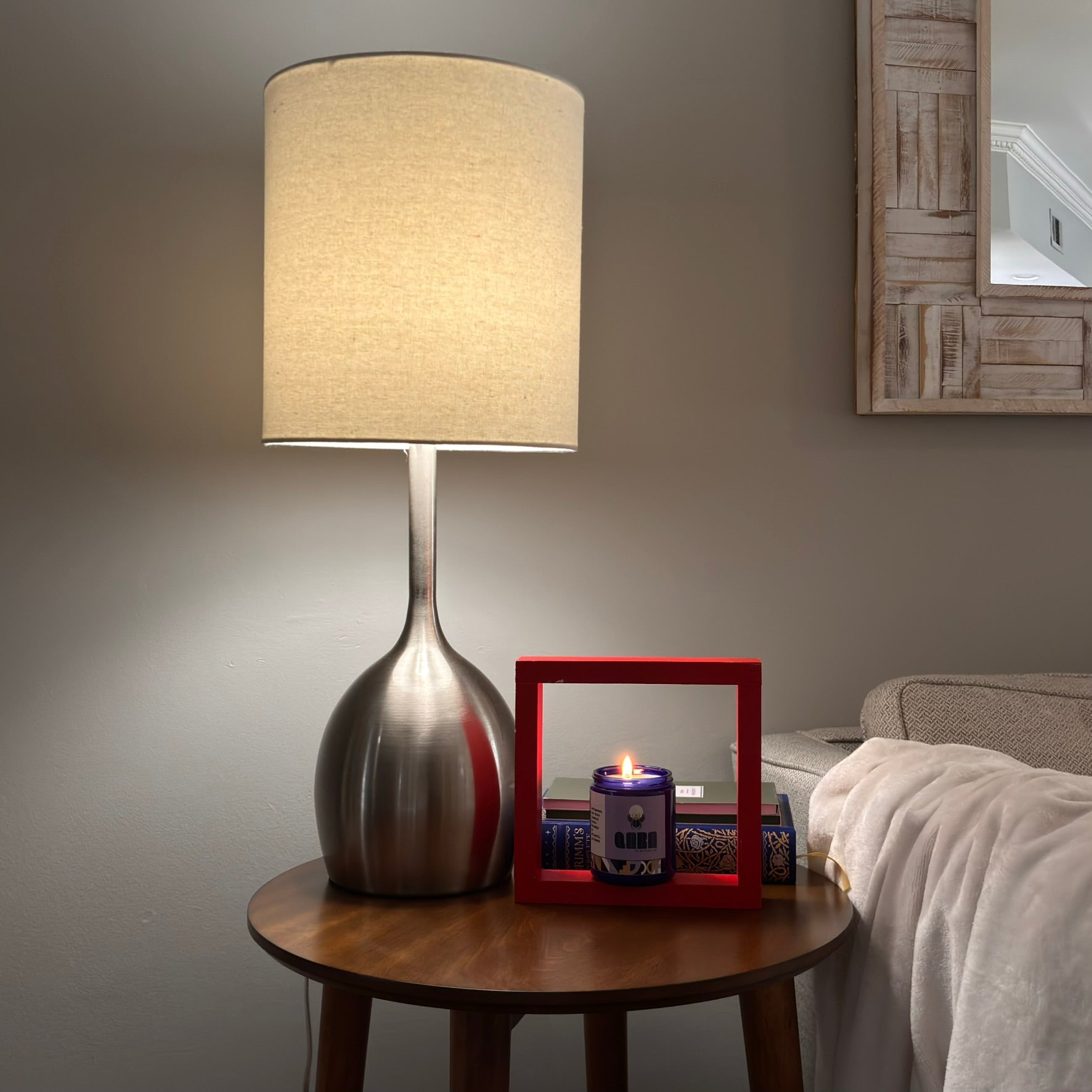 Lamp on a bedside table with a candle and decorative items in a bedroom Candle jar with a purple label featuring the brand 'Qara' on a beige background. QARA IVORY ORIS scented candle Violet Fig  flowery scent luxurious scent natural ingredients and lab tested fragrance oil front cobalt blue jar
