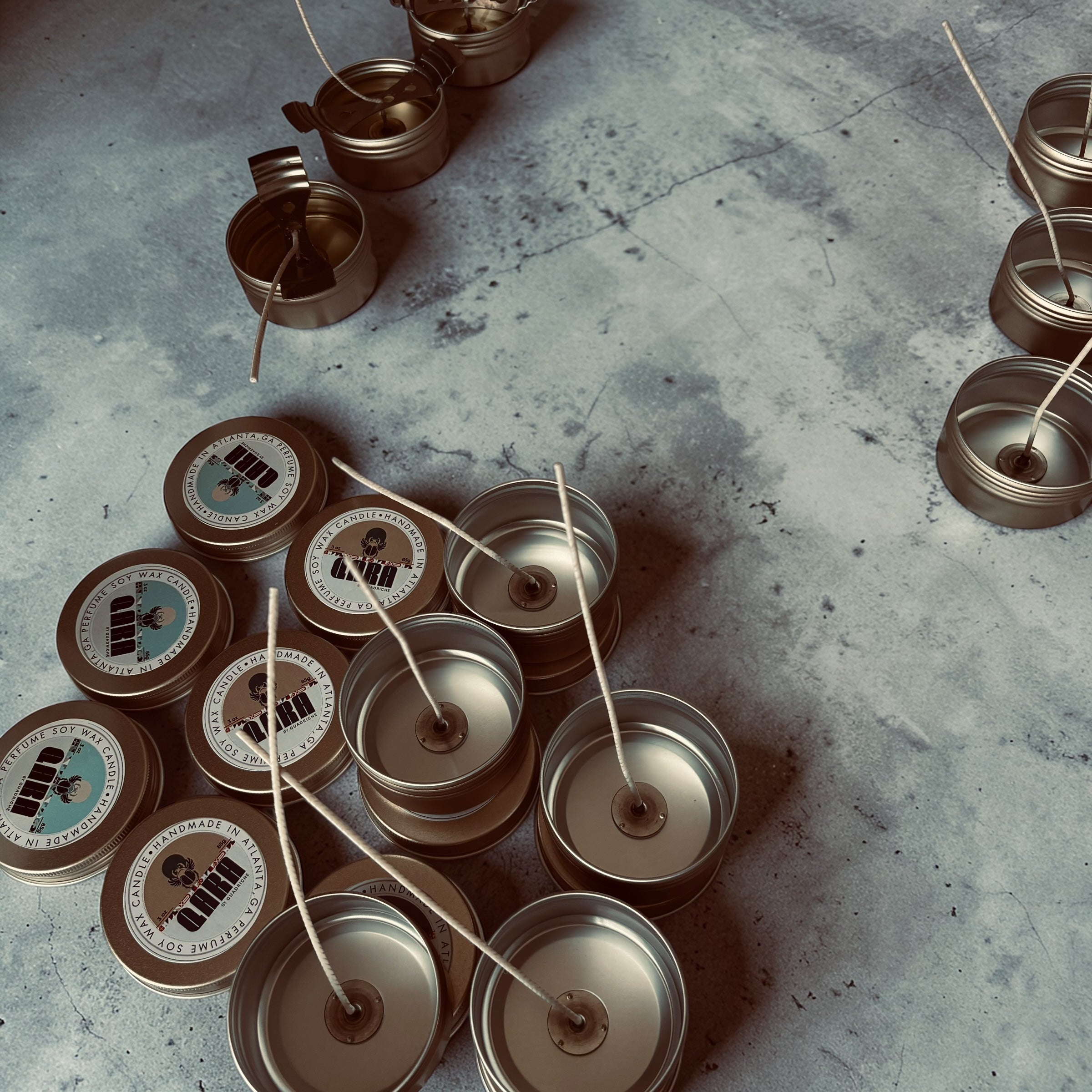 Multiple small metal containers with candles on a concrete surface making process for Quadriche Discovery tin candles