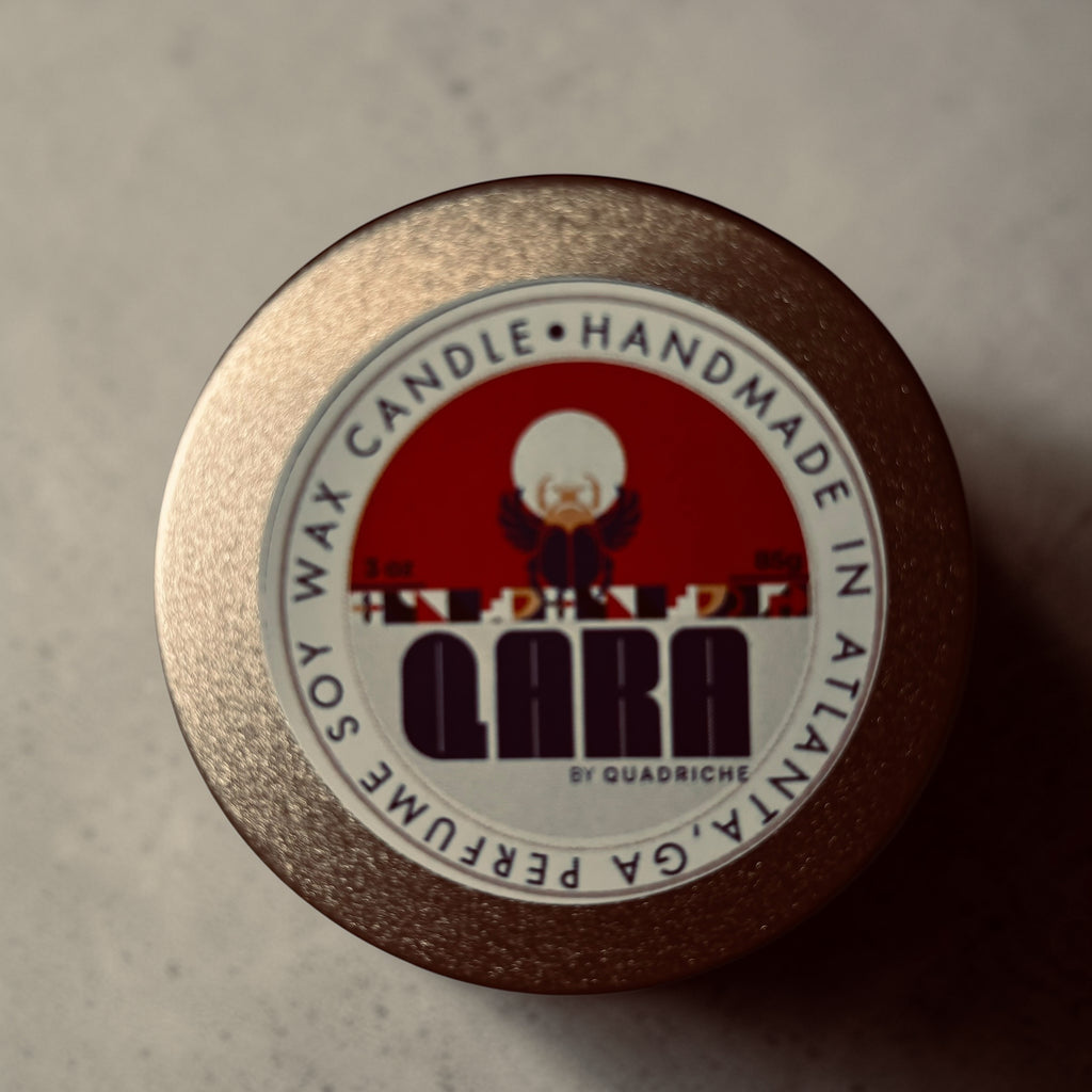 Close-up of aQuadriche coconut soy wax candle label on a textured surface in a champagne gold tin 3oz discovery travel candle