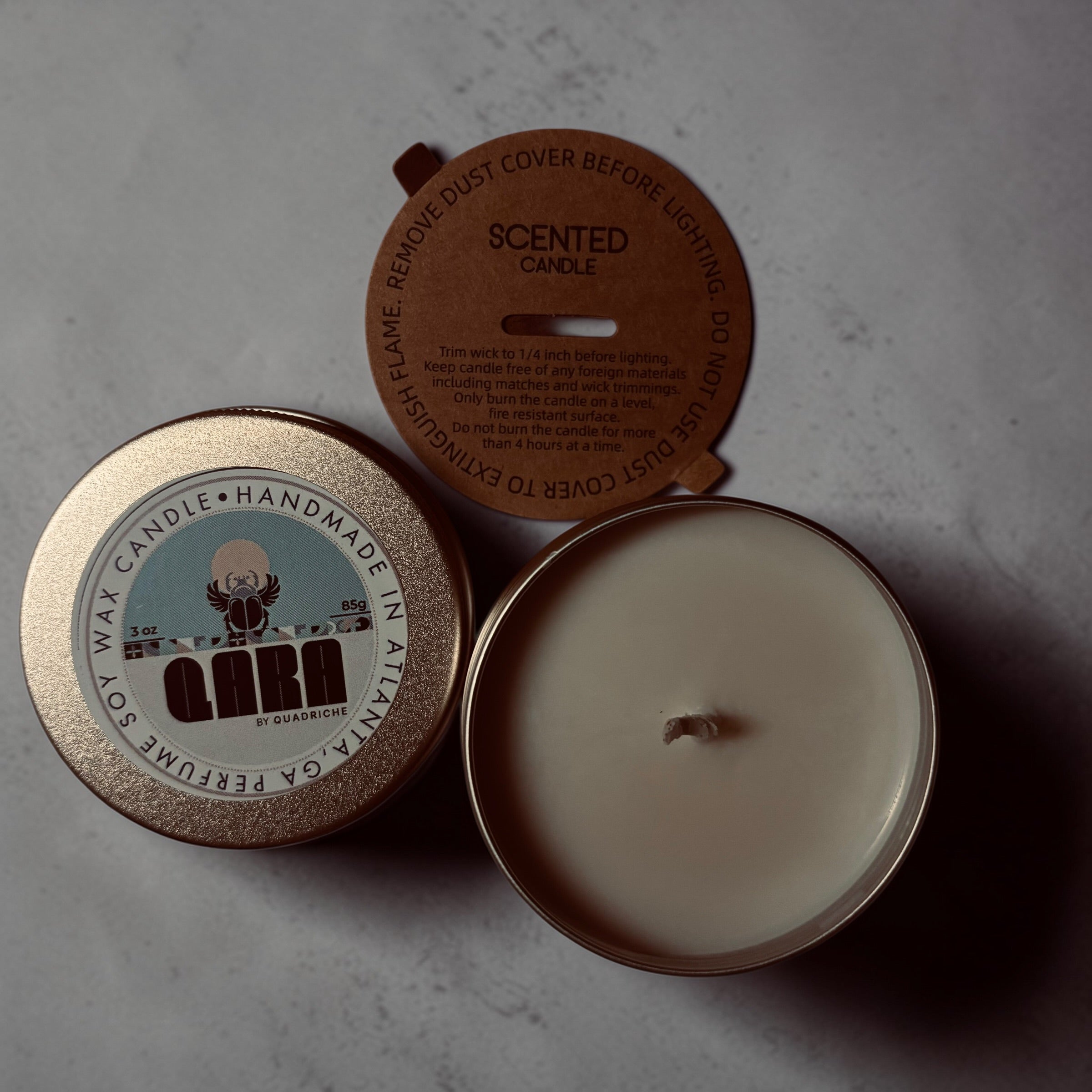 Scented candle with a lid showing branding on a gray surface Dew Discovery Travel 3oz Candle in a tin with a label on a wooden surface ozone apple eucalyptus scent 