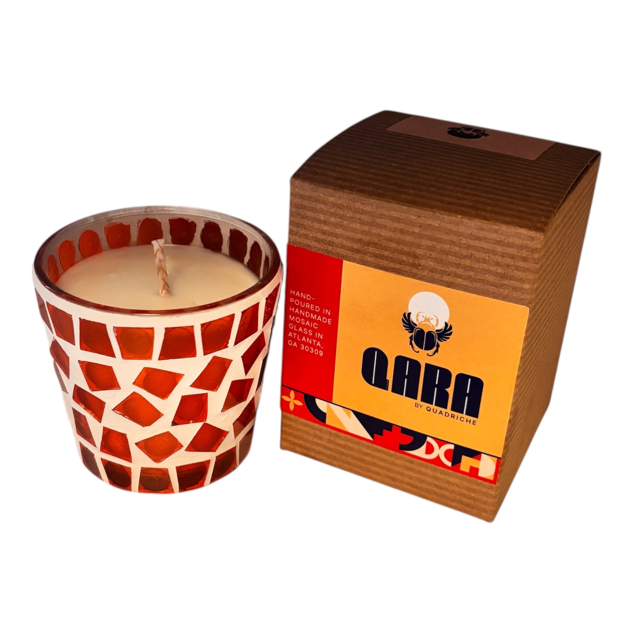Candle in a handmade mosaic glass holder next to its packaging box on a white background