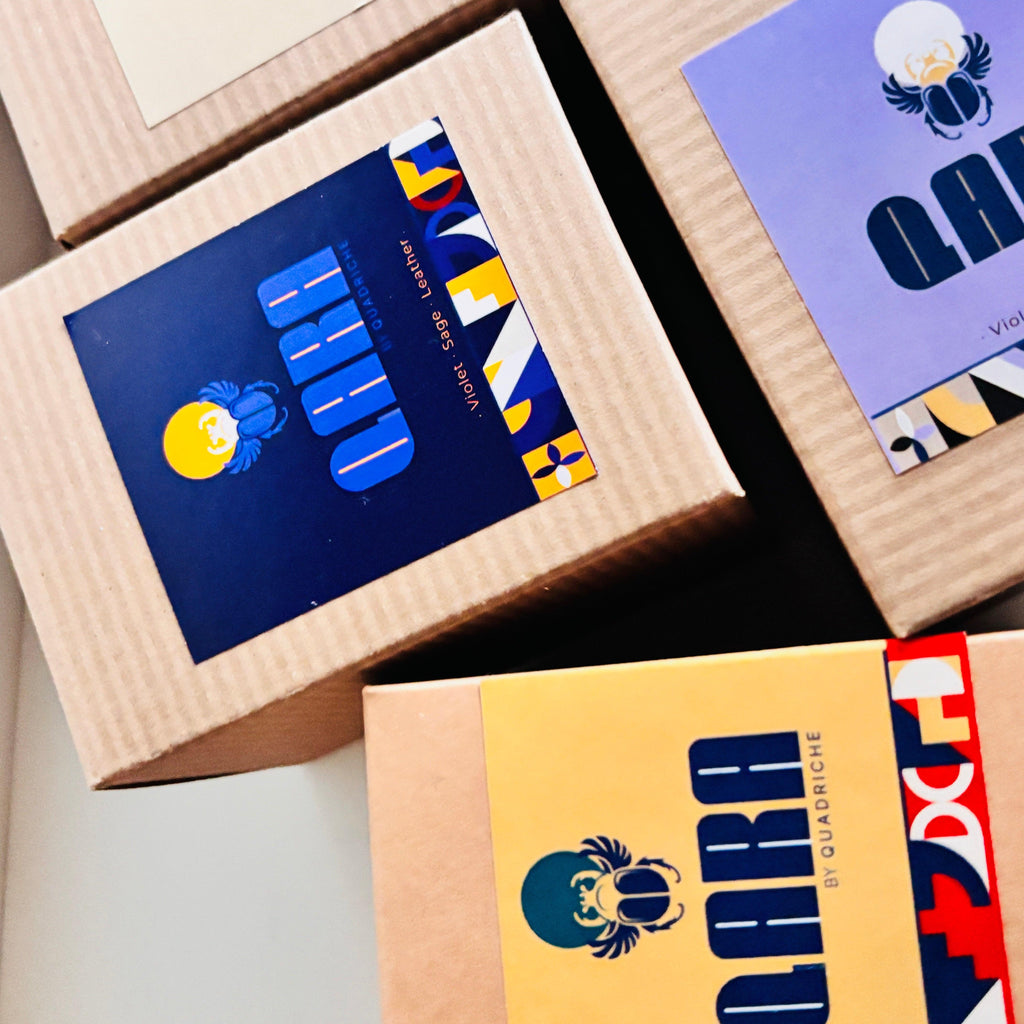 Kraft paper boxes with colorful labels on a flat surface reading 'QARA by Quadriche.'