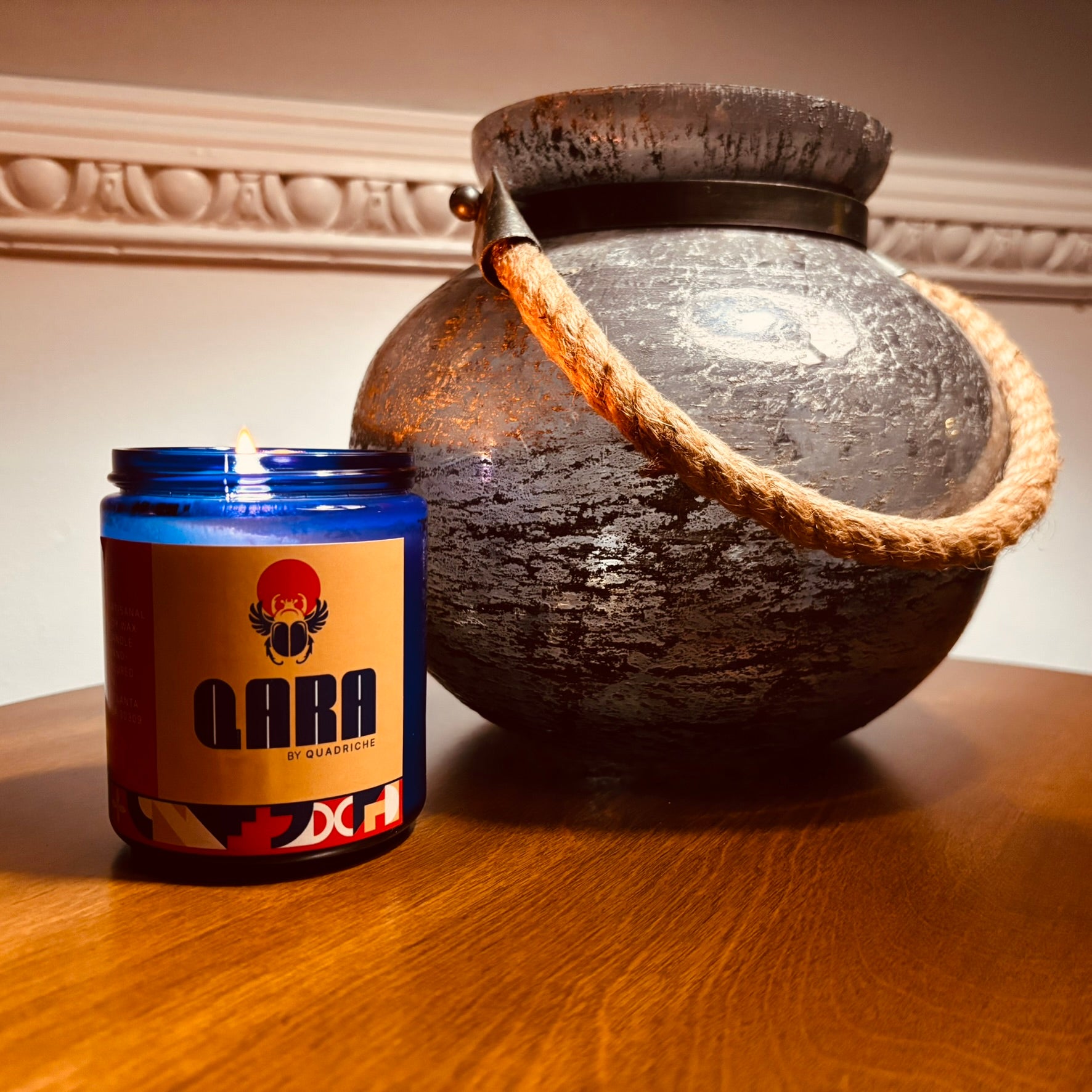 QARA supplement container next to a large decorative pot on a wooden surface.