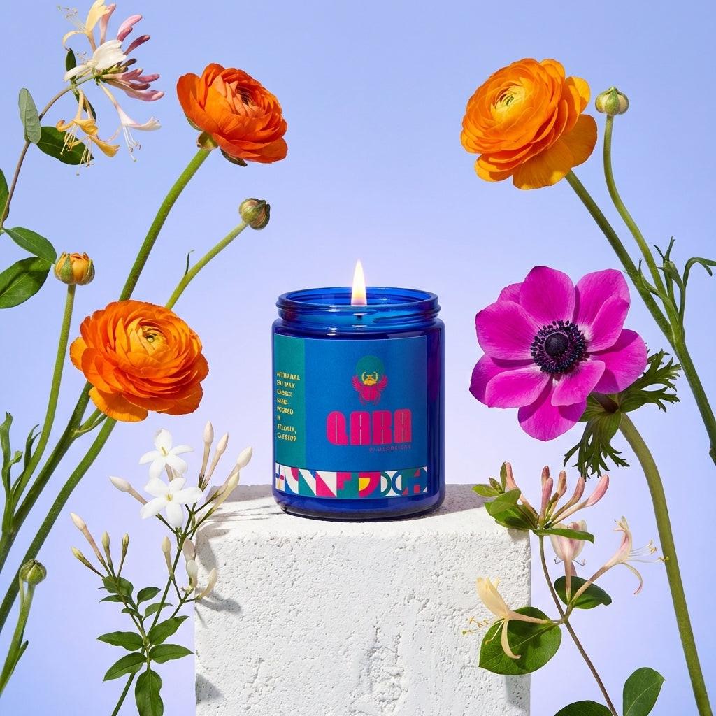 Cobalt blue glass jar candle by Quadriche with colorful label surrounded by vibrant flowers on a light blue background. Seventh Bloom is a jasmine scented candle.