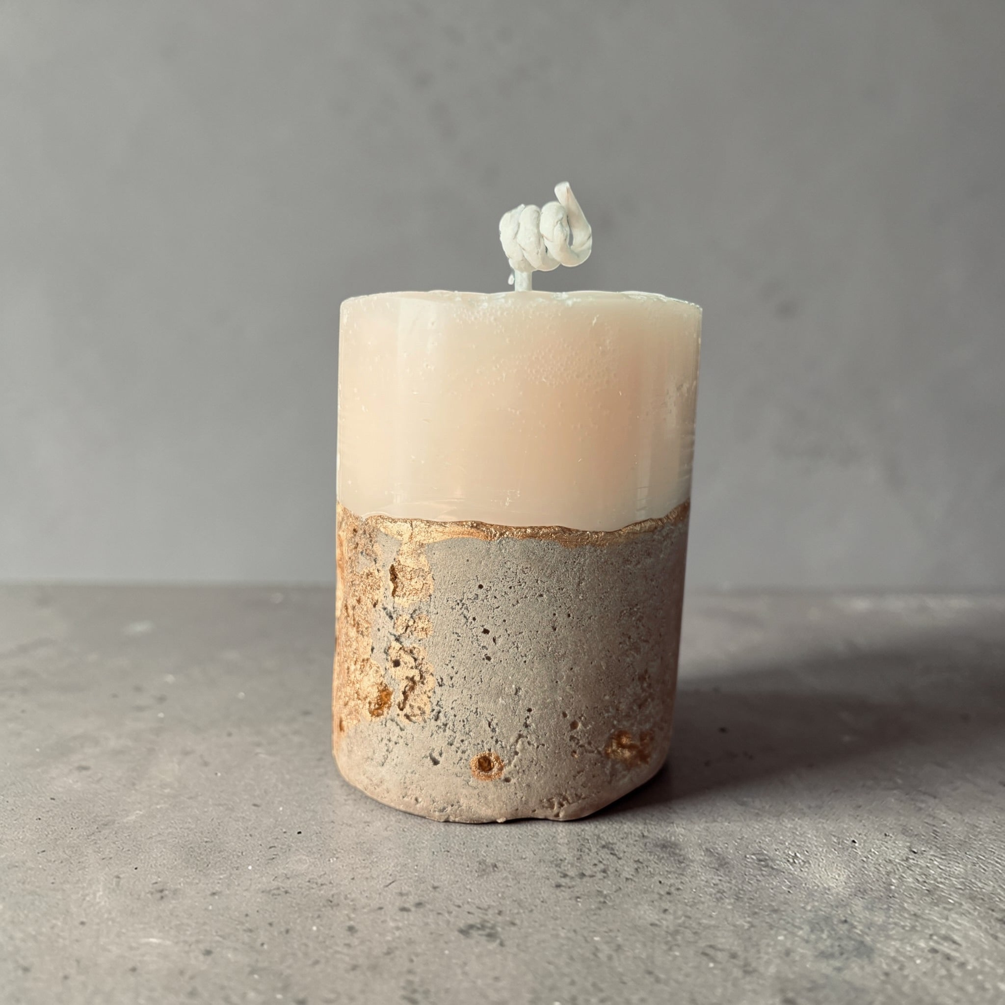 Tall stacked wax concrete candle with textured stone base and gold detailing, modern sculptural home fragrance candle